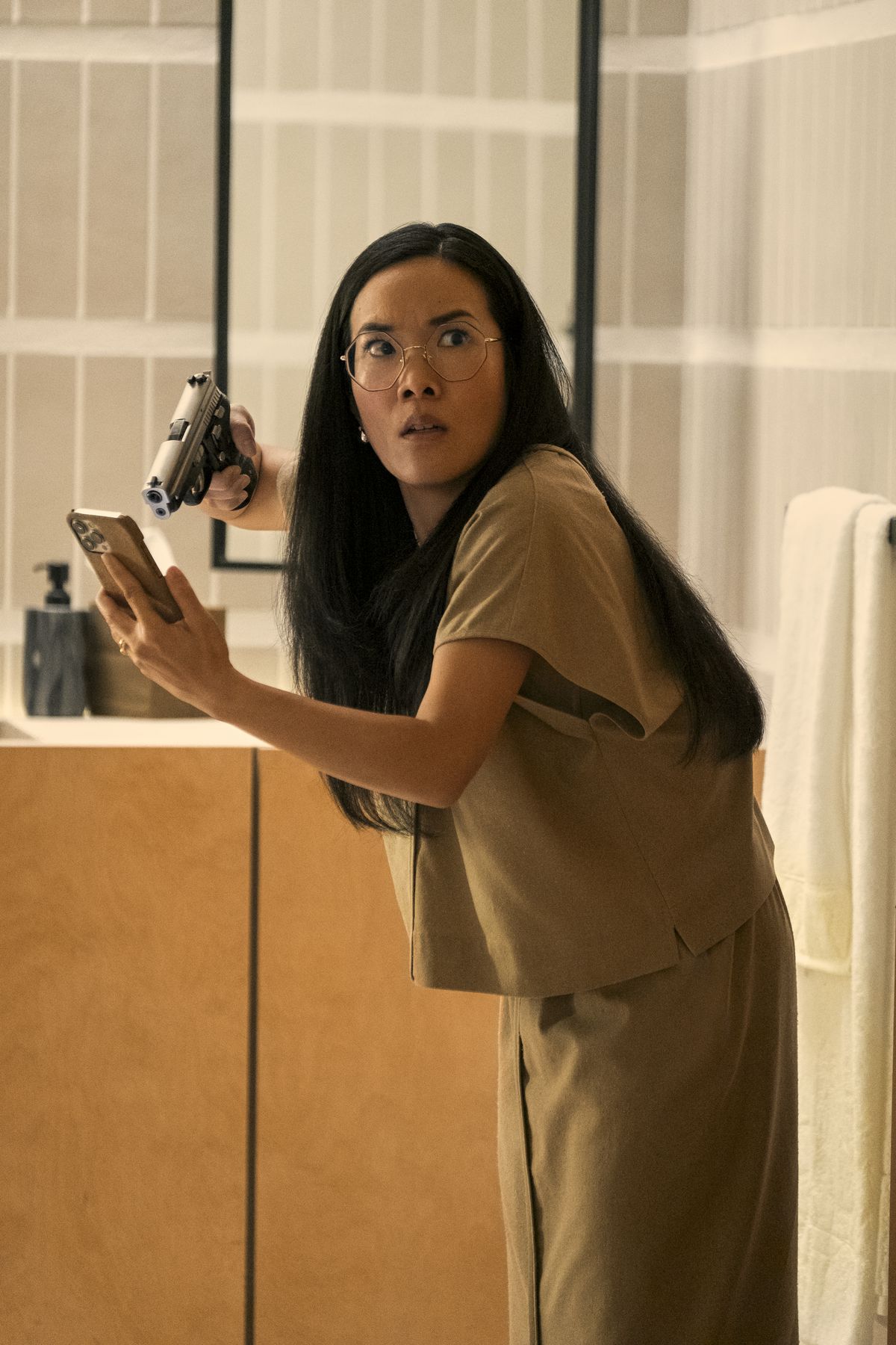 Amy (Ali Wong) håller en pistol mot en telefon i handen och ser chockad på något utanför kameran