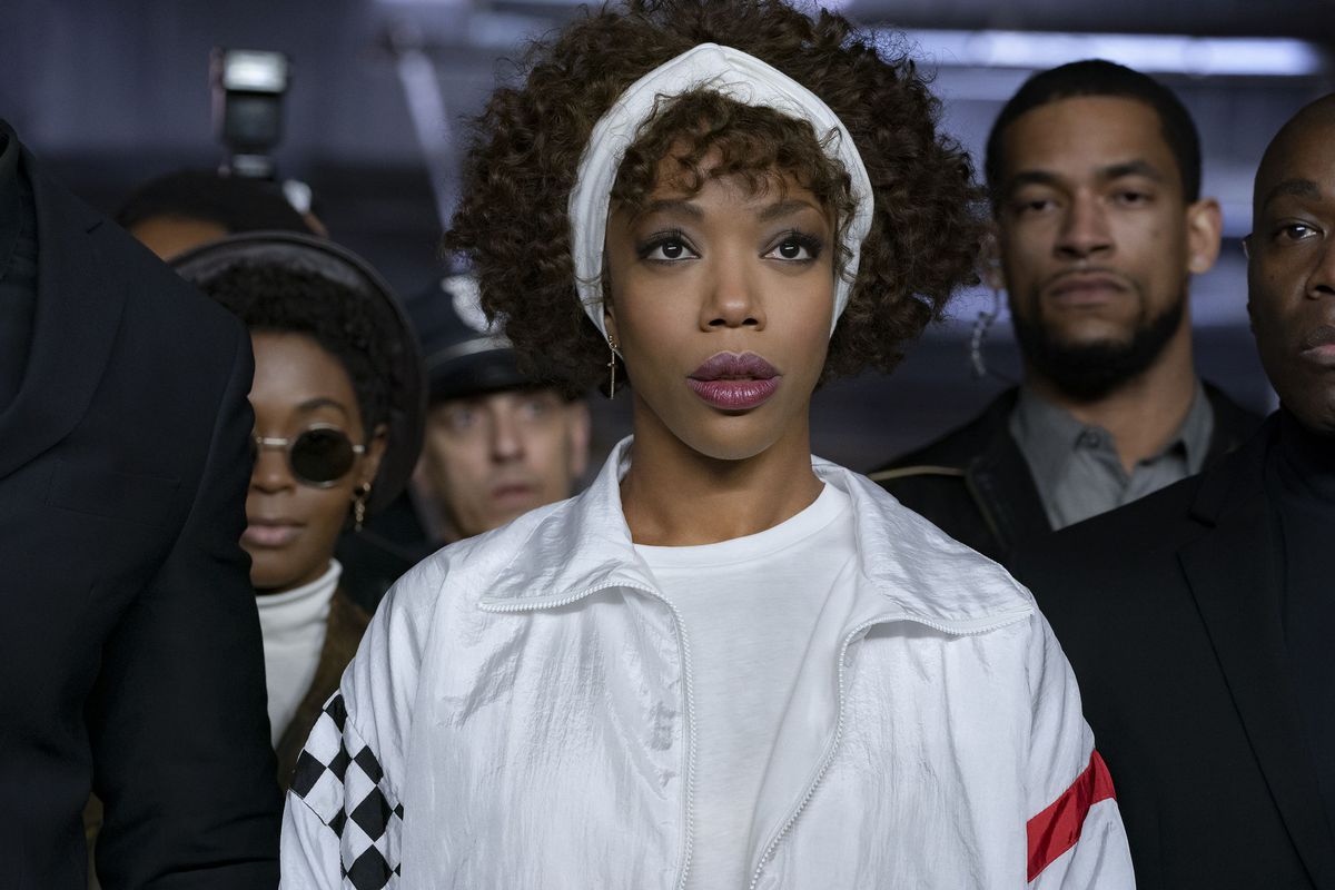 Naomi Ackie bär helvitt, med ett vitt pannband, och är omgiven av säkerhetsvakter som Whitney Houston i I Wanna Dance With Somebody.