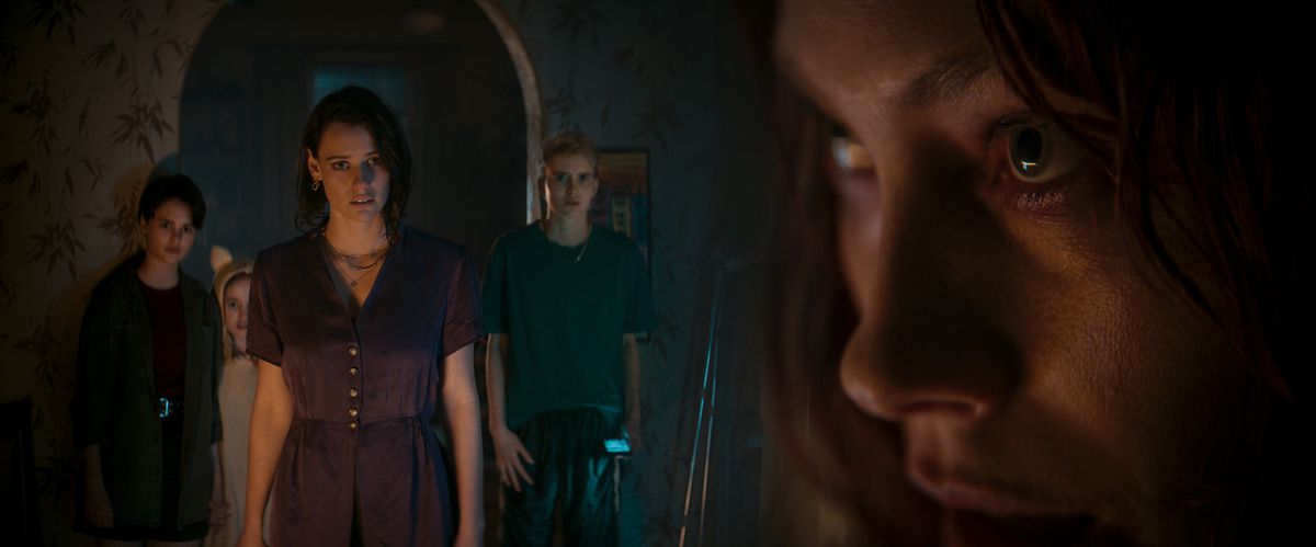 Beth (Lily Sullivan) konfronterar nervöst sin störda syster Ellie (Alyssa Sutherland) när Ellies tre barn kryper bakom henne i en mörk dörröppning i Evil Dead Rise