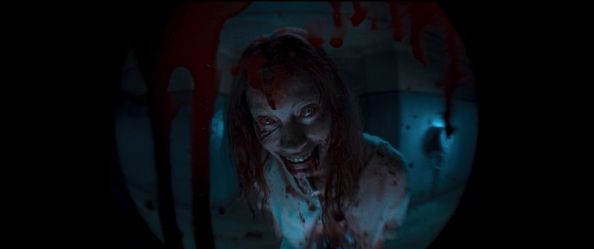 Deaditen Ellie ger ett monstruöst leende från andra sidan av ett blodfläckat titthål i Evil Dead Rise
