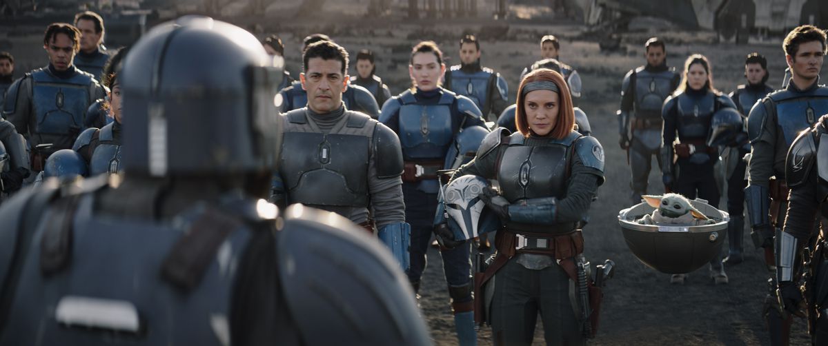 Bo-Katan och flera av hennes Mandalorian-kompisar står framför Paz Vizla med hjälmarna av (och Grogu) i säsong 3 av The Mandalorian.