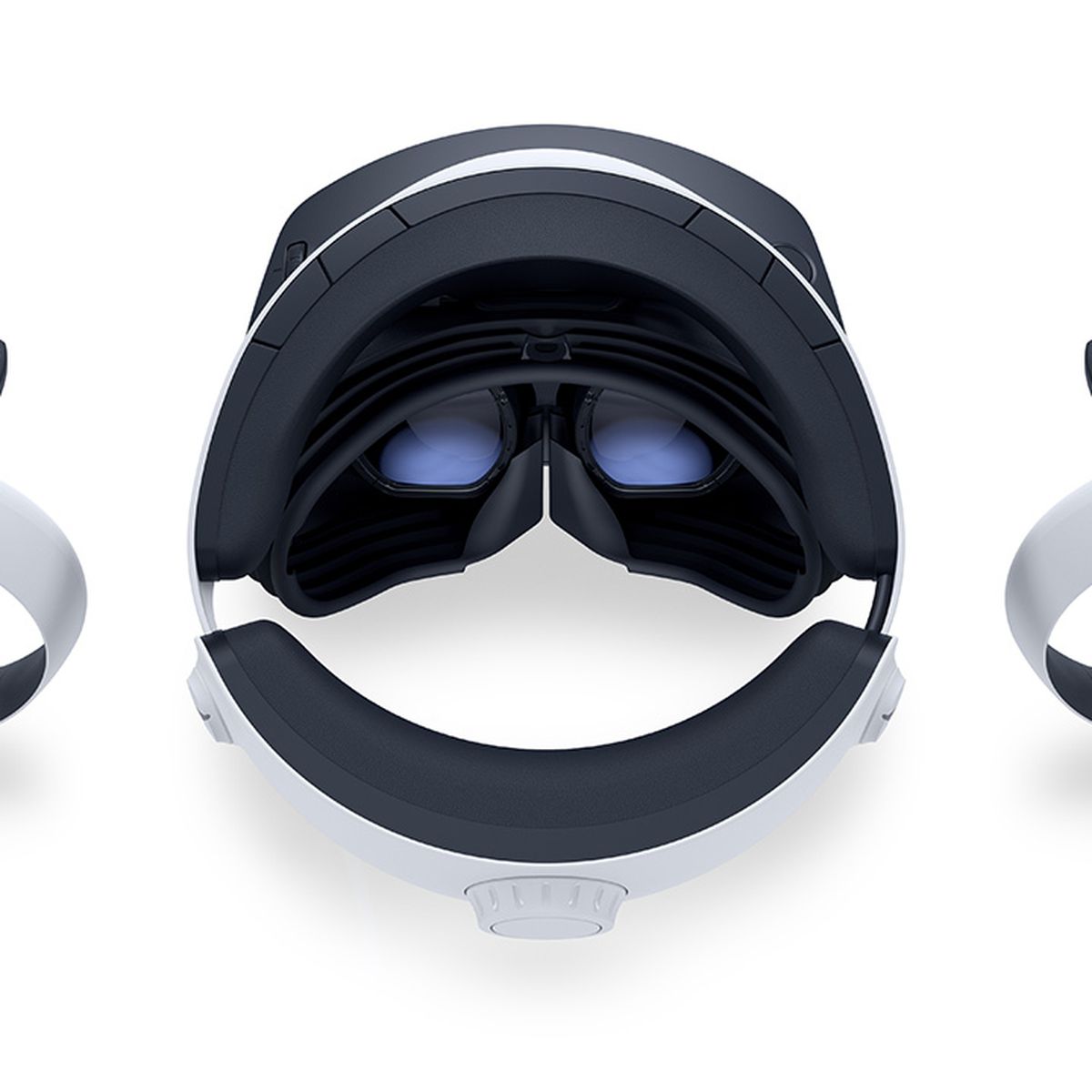 PSVR 2-headsetet, sett från ovan, vilar på en vit yta, flankerad av båda VR2 Sense-kontrollerna