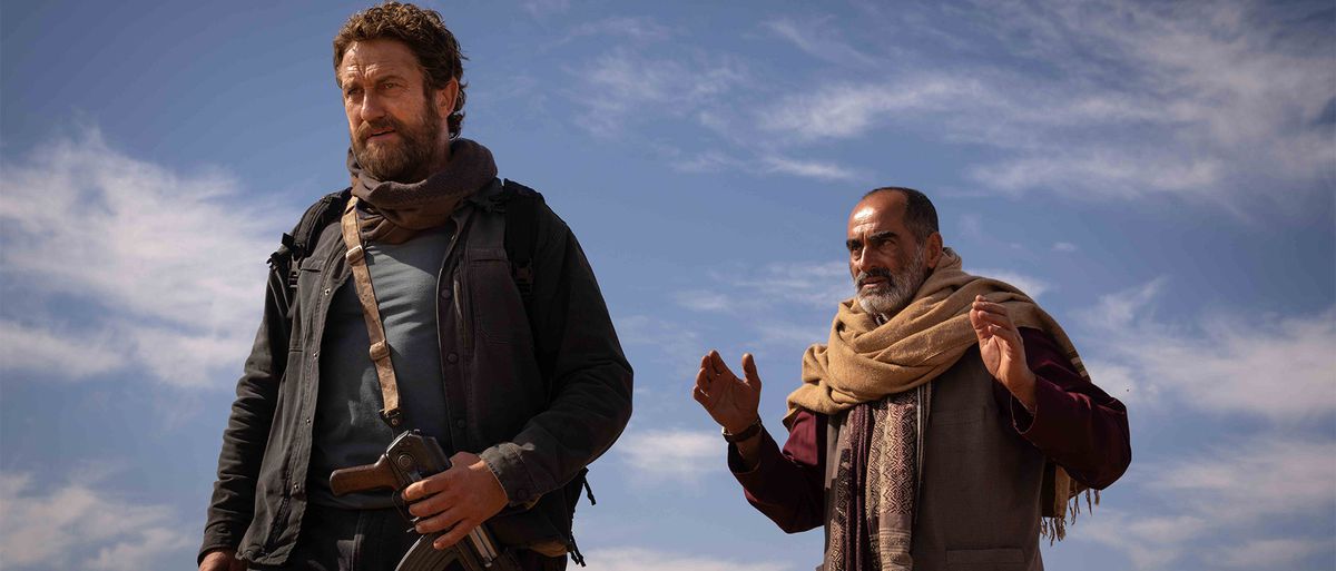 A bearded Navid Negahban gestures at Gerard Butler with a blue sky behind them in Kandahar.