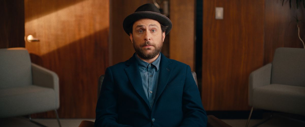 Charlie Day looks surprised while wearing a suit and hat while sitting in a chair in an office in Fool’s Paradise.