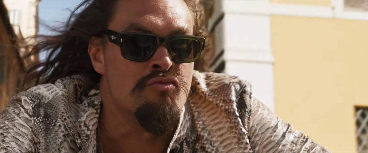 Jason Momoa purses his lips while wearing sunglasses and a snakeskin jacket in the Fast X trailer.