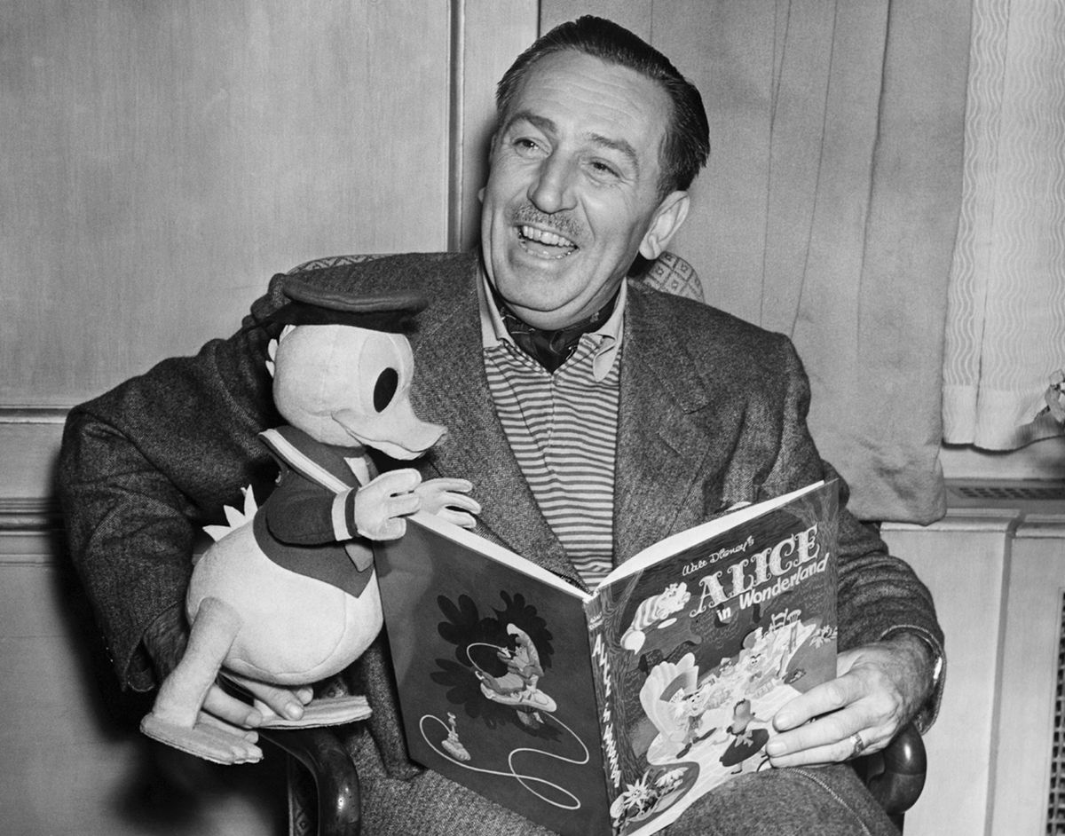 I ett svartvitt porträtt från 1951 håller Walt Disney en uppstoppad Kalle Anka i sitt knä när han läser från en kopia av Alice i Underlandet