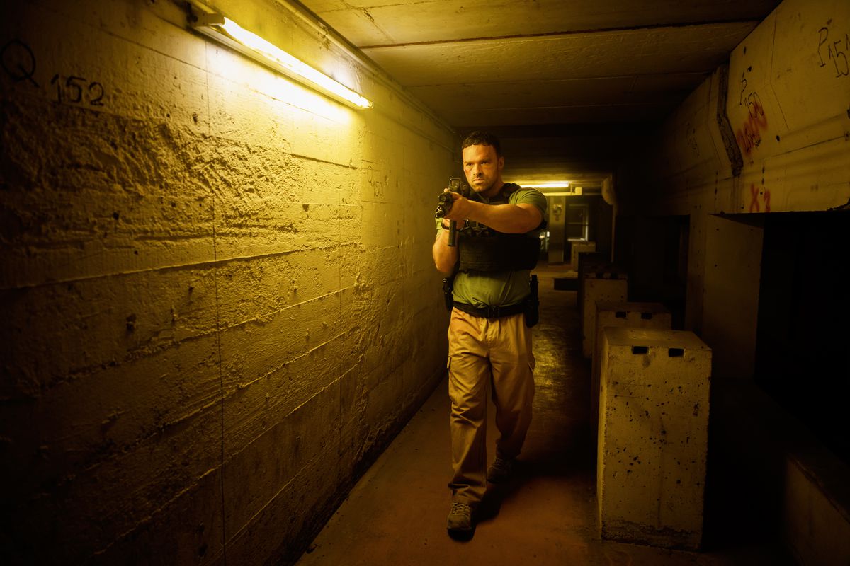 Alban Lenoir går genom en lång hall medan han håller ett automatgevär i AKA.