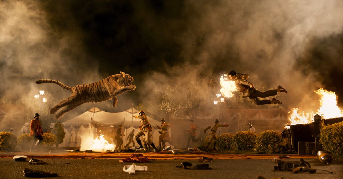 A tiger and an Indian man with a crew cut, suspenders, a dress shirt holding a torch leap into the air at each other while soldiers cower behind them in RRR