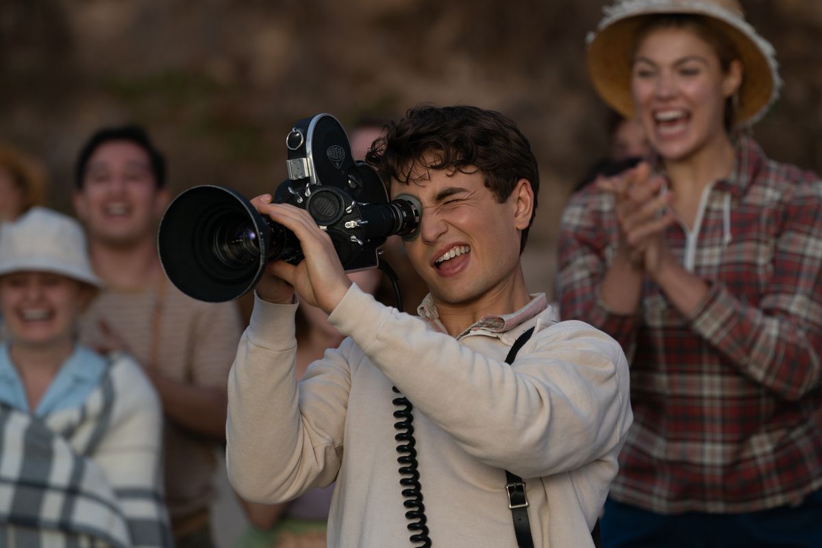 Tonåringen Sammy Fabelman (Gabriel LaBelle) flinar när han riktar en stor filmkamera mot något utanför skärmen medan vuxna bakom honom ler och hejar i The Fabelmans
