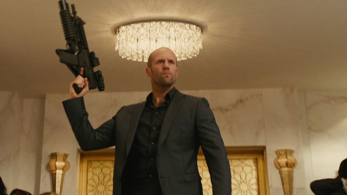 Jason Statham riktar ett automatgevär i luften framför en ljuskrona i Furious 7.