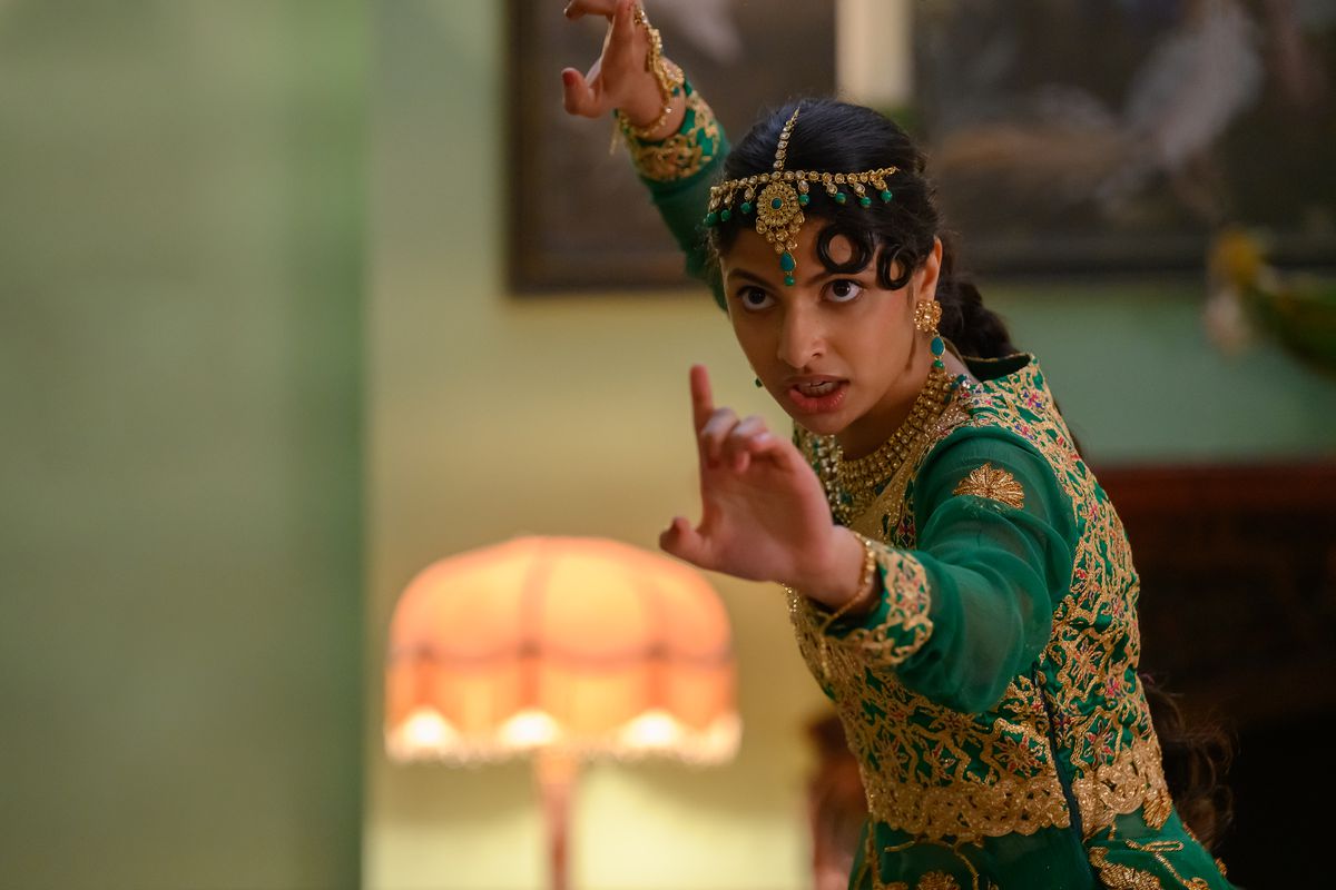 Ria, a Pakistani teenager in a traditional green and gold dance outfit, holds her arms out in a fighting stance.