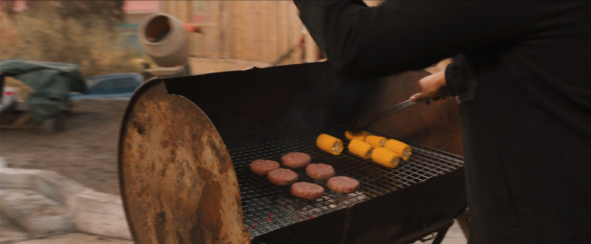 En närbild på grillen i F9: The Fast Saga, med sex råa hamburgerbiffar på och sex tillhörande majskolvar