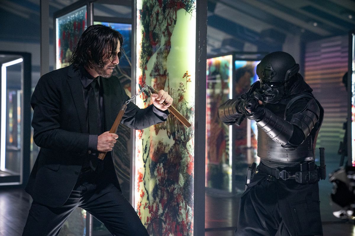 Keanu Reeves som John Wick som håller num-chuks bakom en glaspanel som förbereder sig för att lägga ett bakhåll i en soldat i svart samurajrustning i John Wick: Chapter 4.