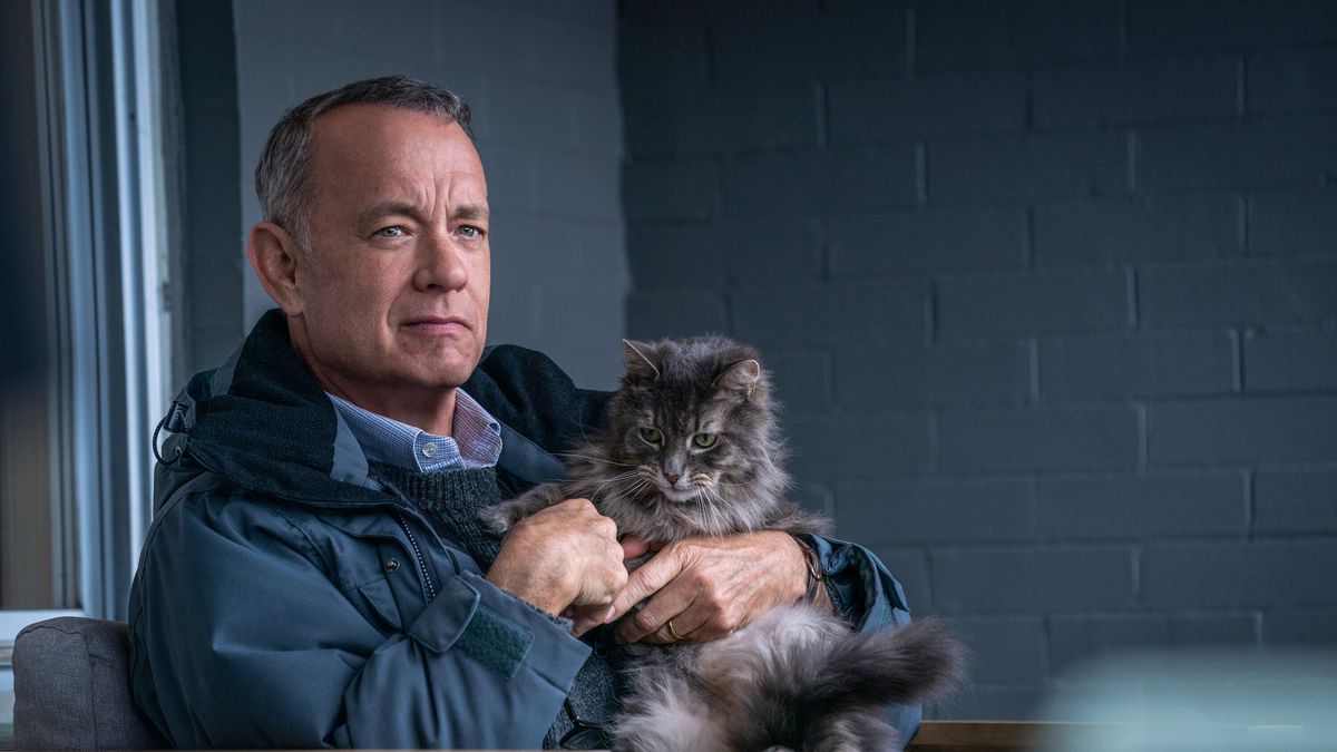 Otto (Tom Hanks) sitter på sin veranda och håller i en katt med ett knappt synligt leende på läpparna.