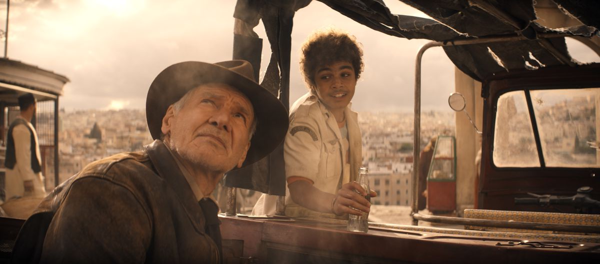 Indiana Jones (Harrison Ford) tittar upp mot en mulen grå himmel medan en grinande tonåring (Ethann Isidore) försöker prata med honom när han rustar för en tur i sin lastbil i Indiana Jones and the Dial of Destiny