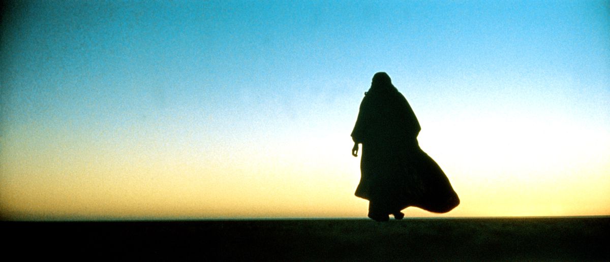 A man in traditional Bedouin dress is silhouetted against a desert sunset sky