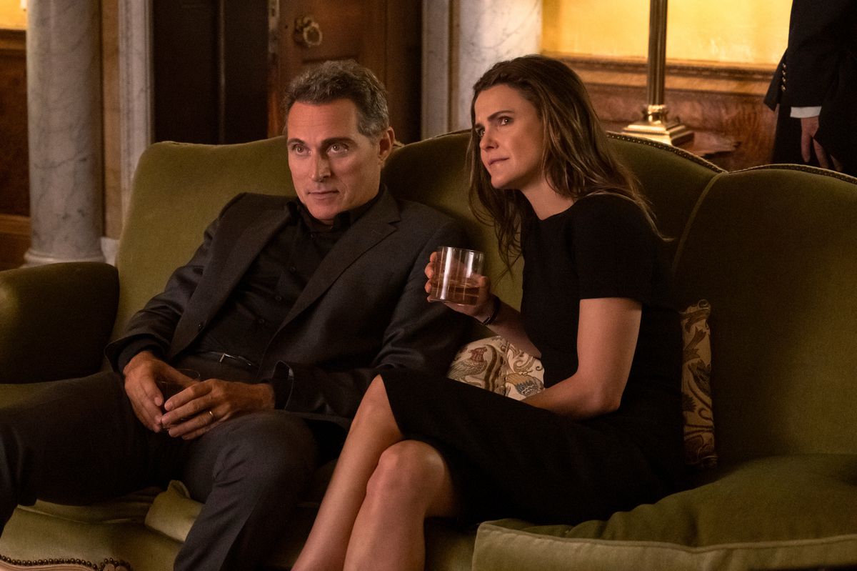 Keri Russell and Rufus Sewell sit next to each other on a fancy couch while holding drinks and wearing black in The Diplomat.