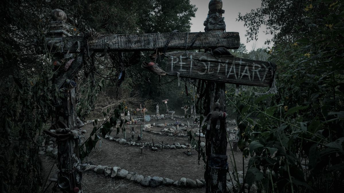 En läskig begravningsplats i skogen, med gråa stenar satta i ett spiralmönster på marken, inramad av en förfallen träport med en planka med texten 