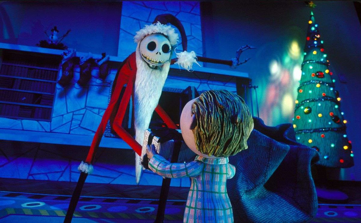 Den höga skelettliknande figuren av Jack i en jultomtedress knäböjer framför en ung pojke i ett vardagsrum med en julgran i bakgrunden i The Nightmare Before Christmas.