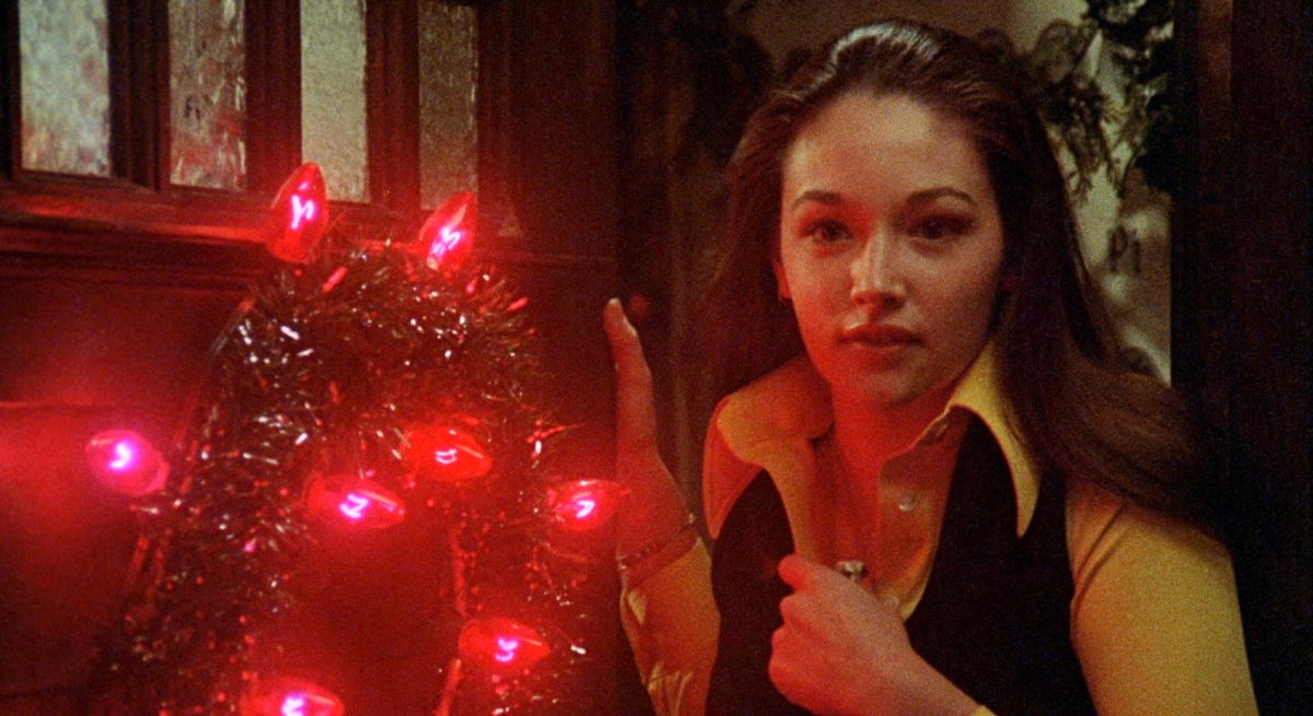 Olivia Hussey stands next to a bright red Christmas wreath in Black Christmas.