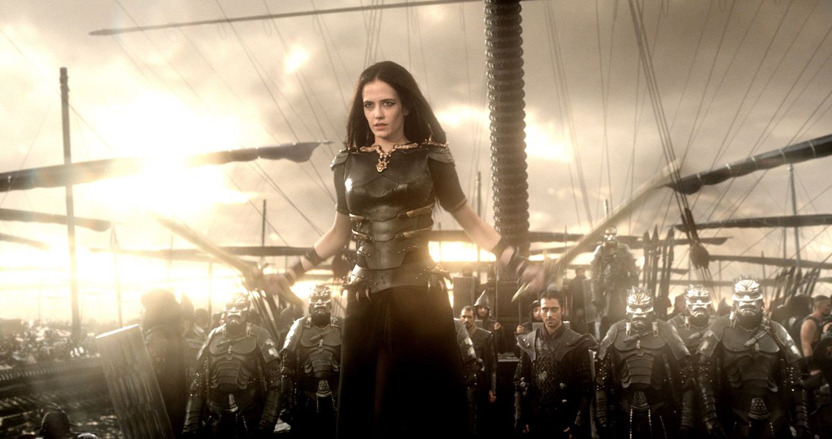 Artemisia (Eva Green) stands with a sword in each hand at the head of an army of men in black armor and silver face masks on the deck of a ship surrounded by other ships in 300: Rise of an Empire