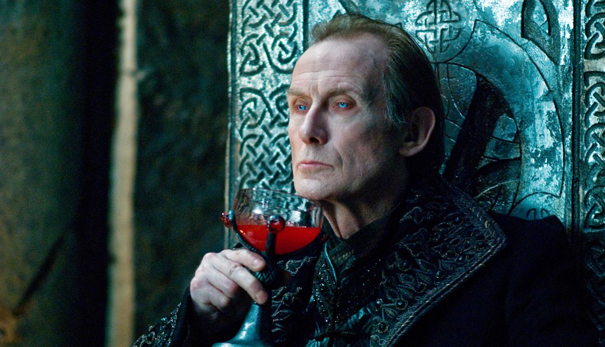 Viktor the ancient vampire (Bill Nighy, in black brocade and with slightly glowing ice-blue eyes) sits on a stone throne carved with Celtic knotwork and drinks bright red blood from a goblet that looks like a glass cup held in a black claw in Underworld: Rise of the Lycans 