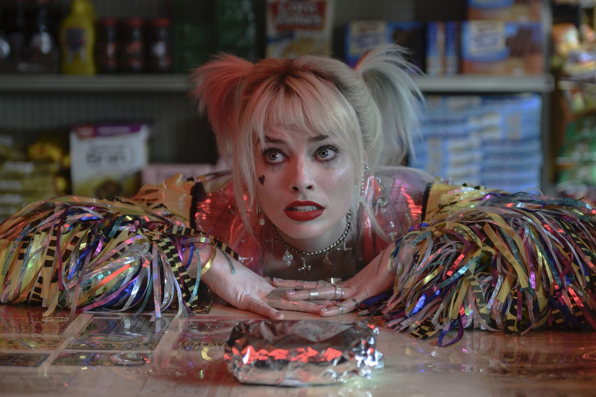 Margot Robbie vilar armarna på en delikatessbänk och tittar bönfallande på sin frukostmacka som Harley Quinn i Birds of Prey.