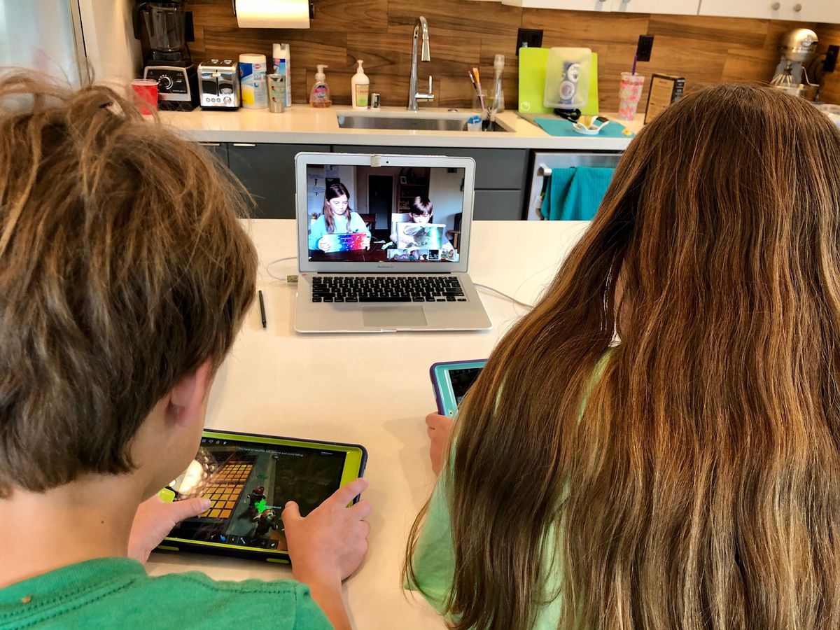 Två barn spelar Roblox på mobila enheter, medan en bärbar dator ansluter dem till ett Hangout-samtal med sina vänner
