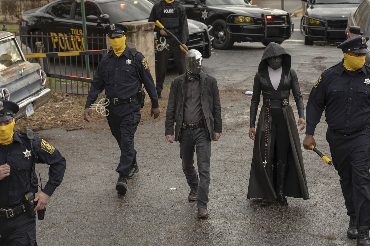 i Watchmen, vigilantes Looking Glass (Tim Blake Nelson) och Sister Night (Regina King) går in i en brottsplats som flankeras av maskerade poliser