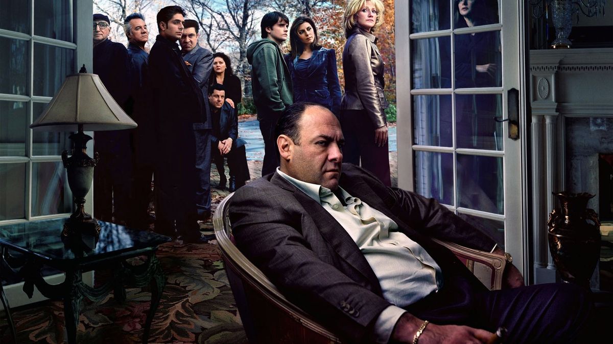 James Gandolfini som mobb-chef Tony Soprano sitter sjunkande i en vardagsrumsstol och glorande utanför skärmen när hans familj och medarbetare samlas och tittar på honom precis utanför sina öppna altandörrar.