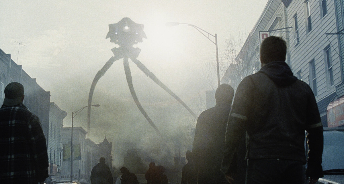 På en grå, rökfylld gata ser en mängd människor med ryggen mot kameran upp på ett enormt främmande stativ som truar över grannskapet i War of the Worlds.