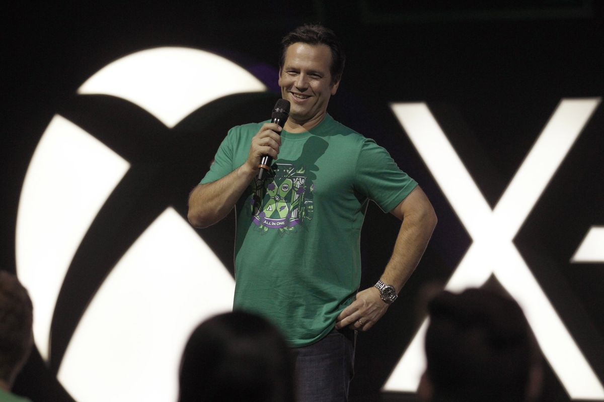 chef för Xbox Phil Spencer som bär en grön T-shirt och håller en mikrofon på scenen med en Xbox-logotyp bakom sig