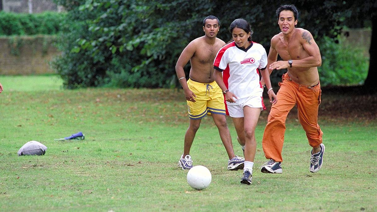 Jess (Parminder Nagra) spelar fotboll i parken med två shirtless män i en skärmdump från Bend it Like Beckham