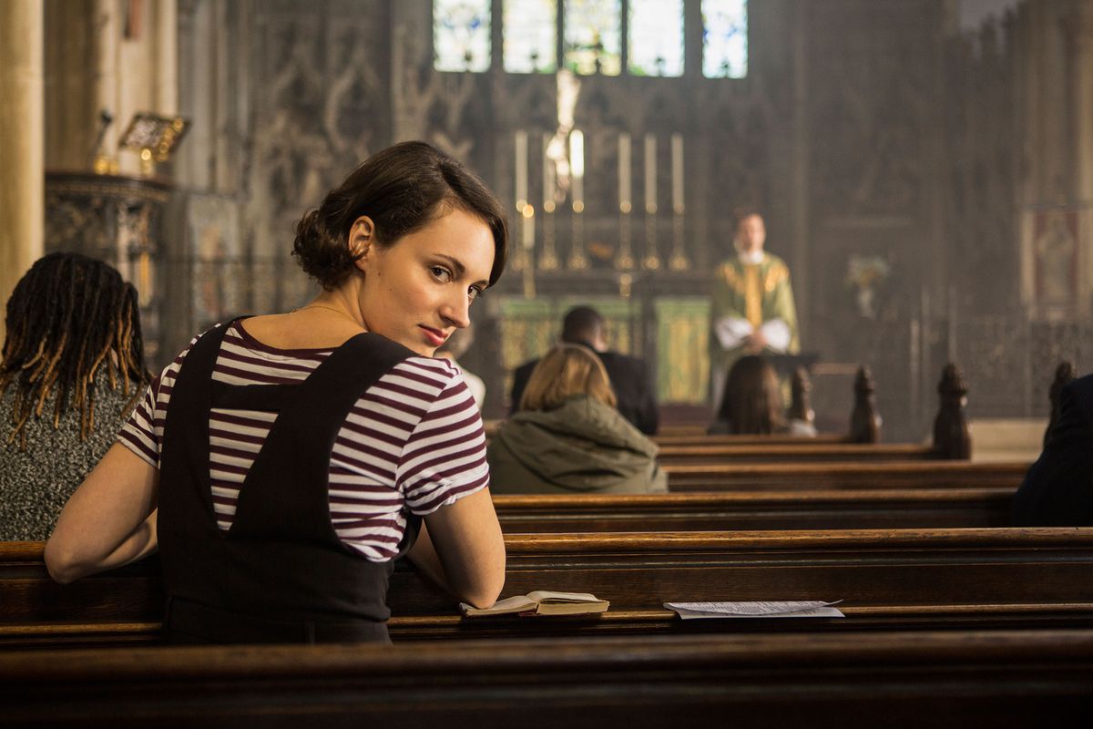 Fleabag (Phoebe Waller-Bridge) casts a knowing glance back over her shoulder as she sits in a pew of a church, listening to a service.
