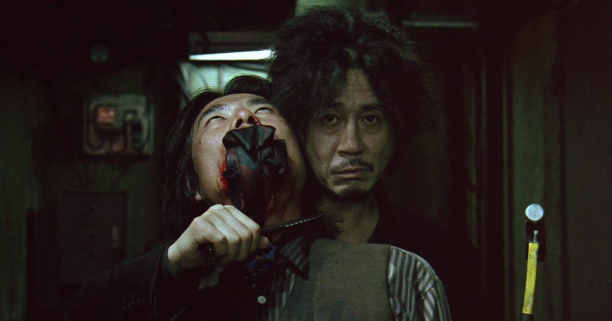 Choi Min-sik som Dae-su Oh håller en gaggad man som gisslan med en kniv och hammare i Oldboy.