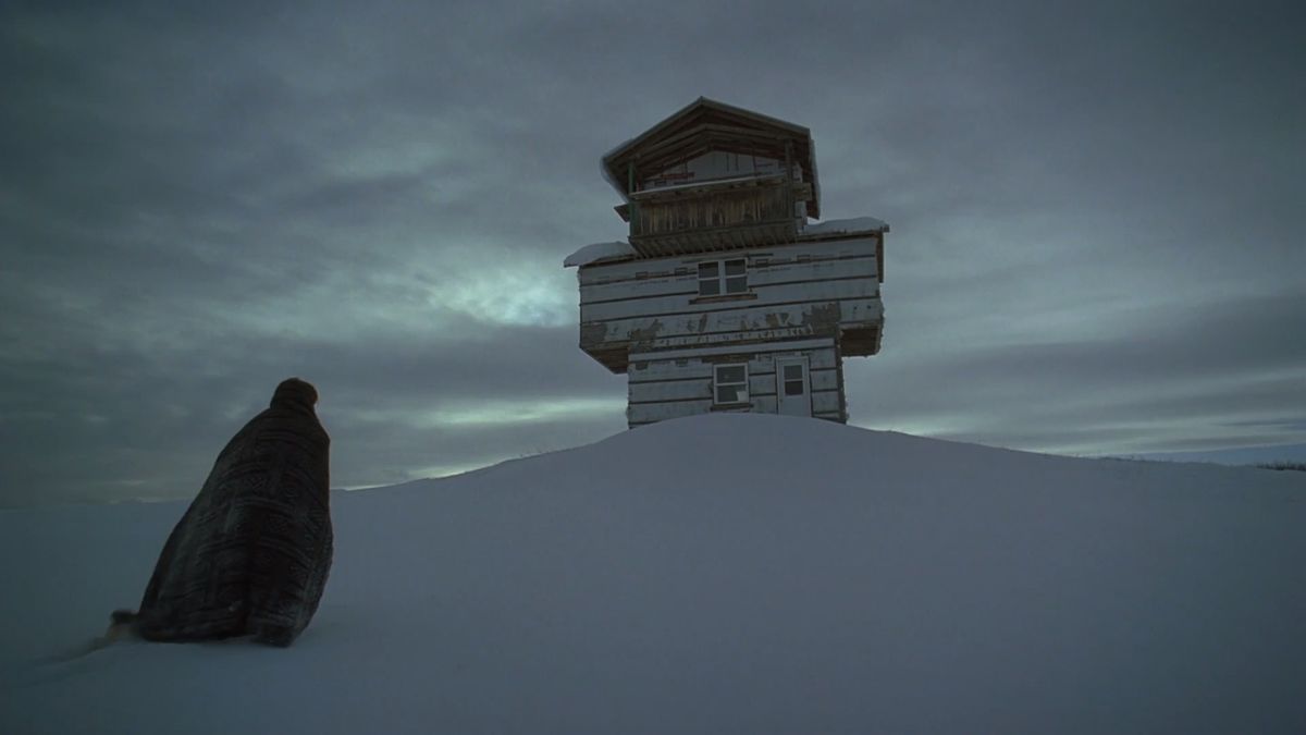 En figur går i snön mot en ensam byggnad i The Lodge