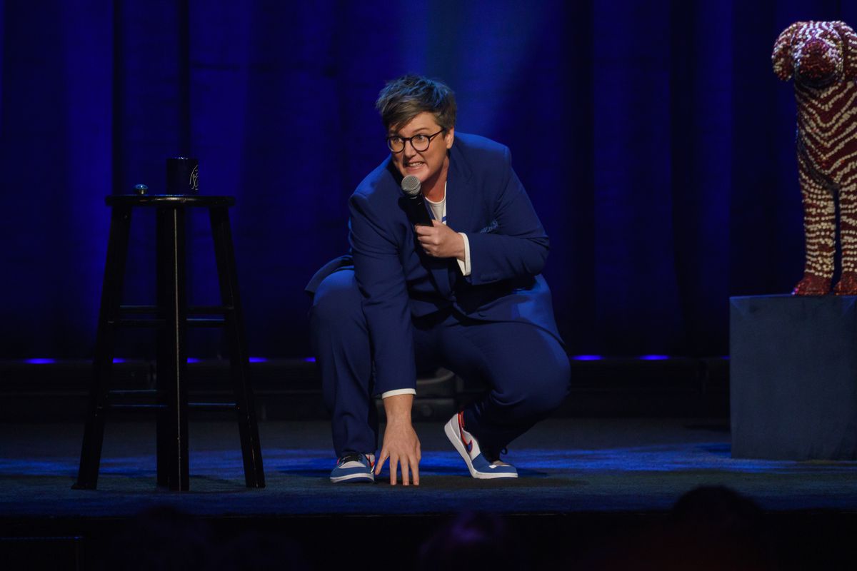 Hannah Gadsby sätter sig ner för att röra golvet med en mikrofon i handen i Douglas