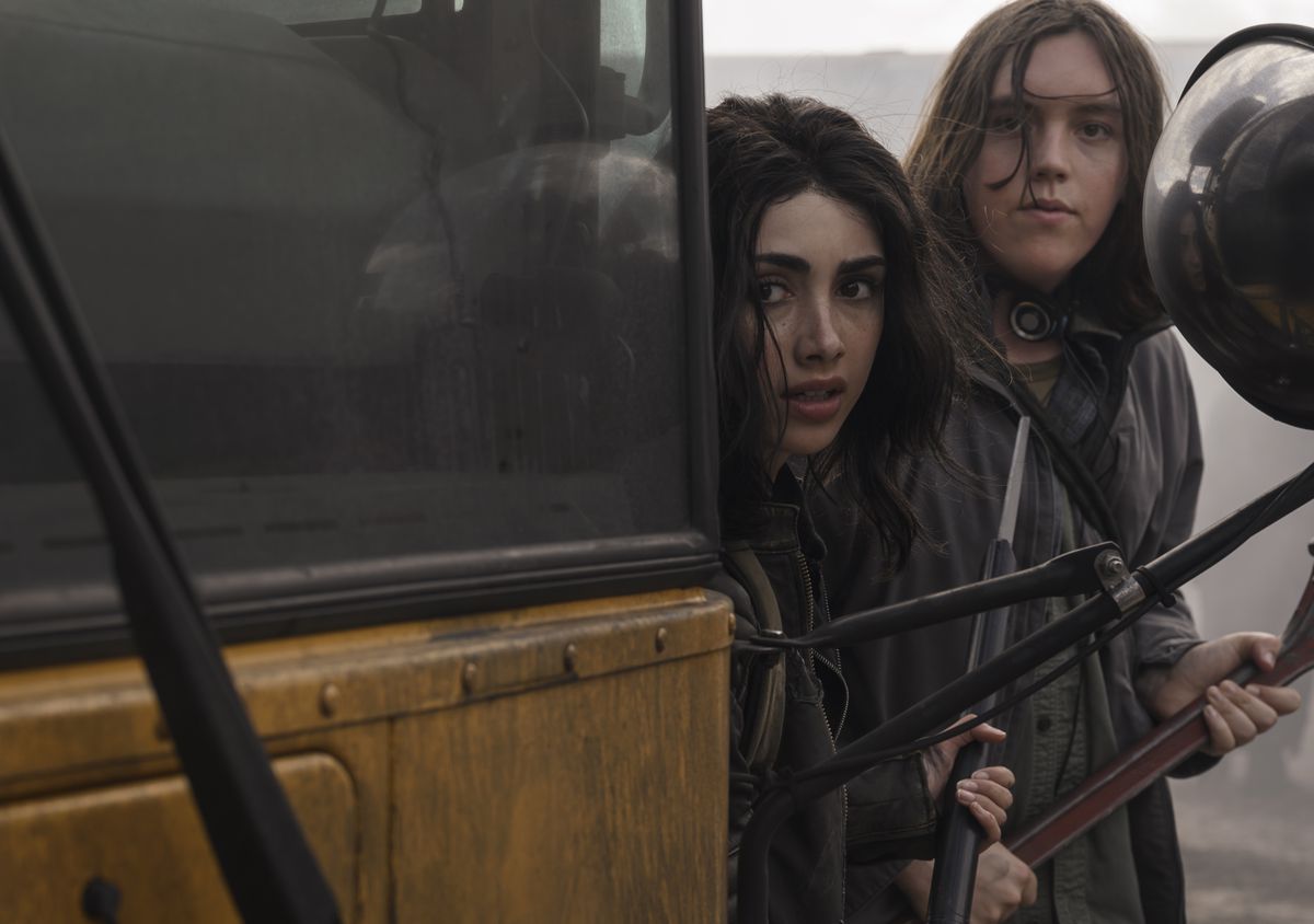 två unga tjejer gömmer sig bakom en skolbuss när de jagar zombier i The Walking Dead: World Beyond