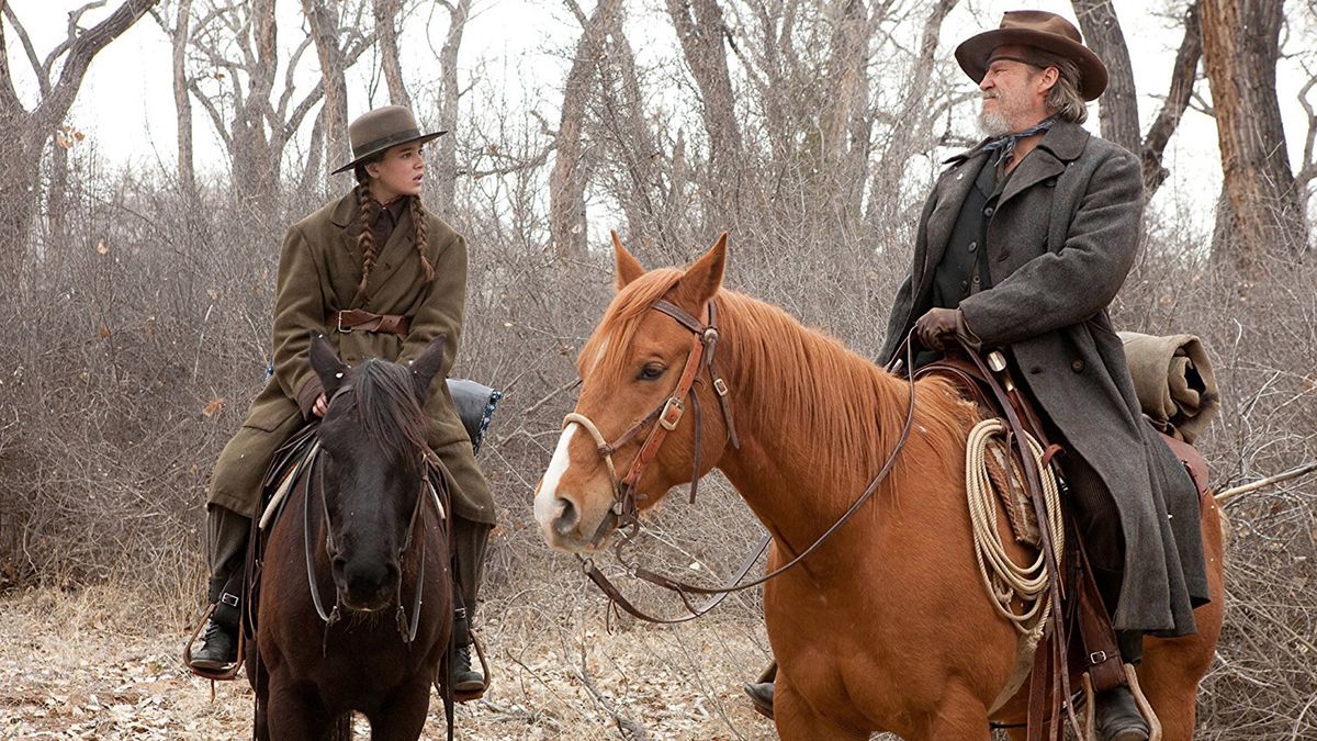 A young girl (Hailee Steinfeld) and an old bearded man (Jeff Bridges) on horses in a forest in True Grit.