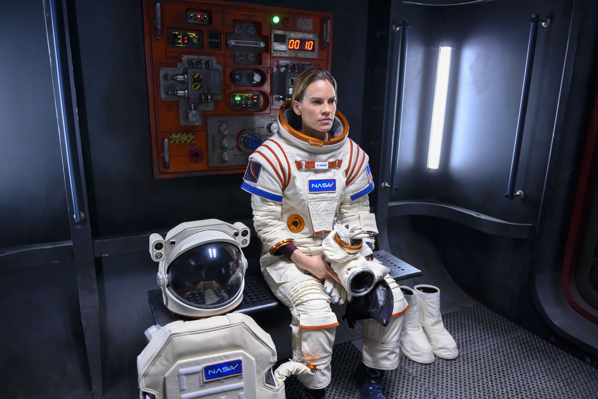 Hilary Swank, i full rymddräkt, sitter och stirrar på en bänk i Netflixs rymdserie Borta.
