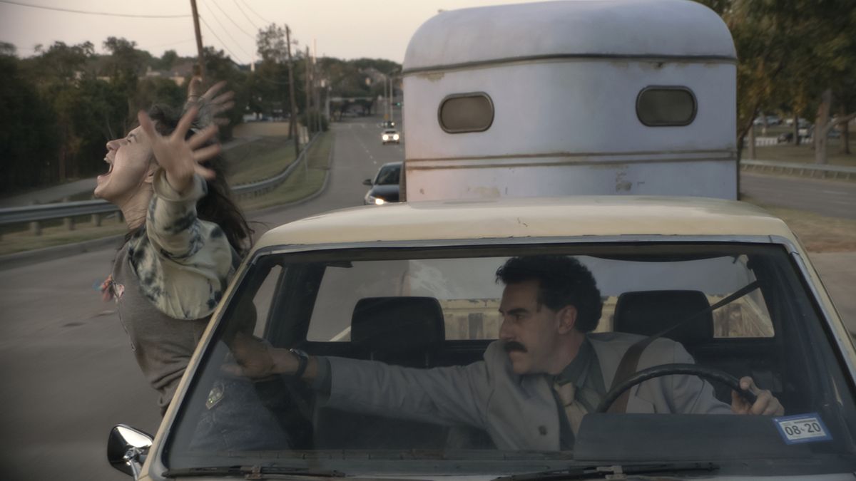 Maria Bakalova lutar sig ut genom fönstret på en rörlig bil när Sacha Baron Cohen försöker dra tillbaka henne i Borat efterföljande Moviefilm