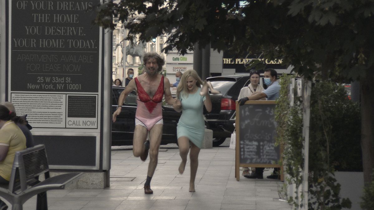 Sacha Baron Cohen, i underkläder och falskt skägg och peruk, springer genom gatorna med Maria Bakalova i Borat Efterföljande Moviefilm