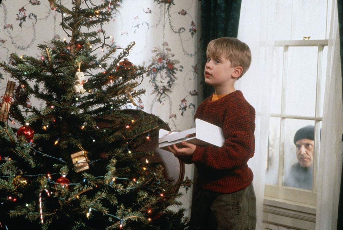 Kevin (Macaulay Culkin) dekorerar ett träd medan Harry (Joe Pesci) tittar genom ett fönster.