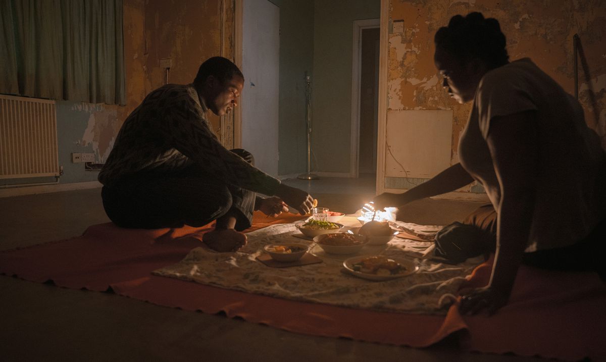 Sudanesiska flyktingar Bol (Sope Dirisu) och Rial (Wunmi Mosaku) äter middag på golvet i sitt omöblerade (och mycket spökade) radhus i hans hus.