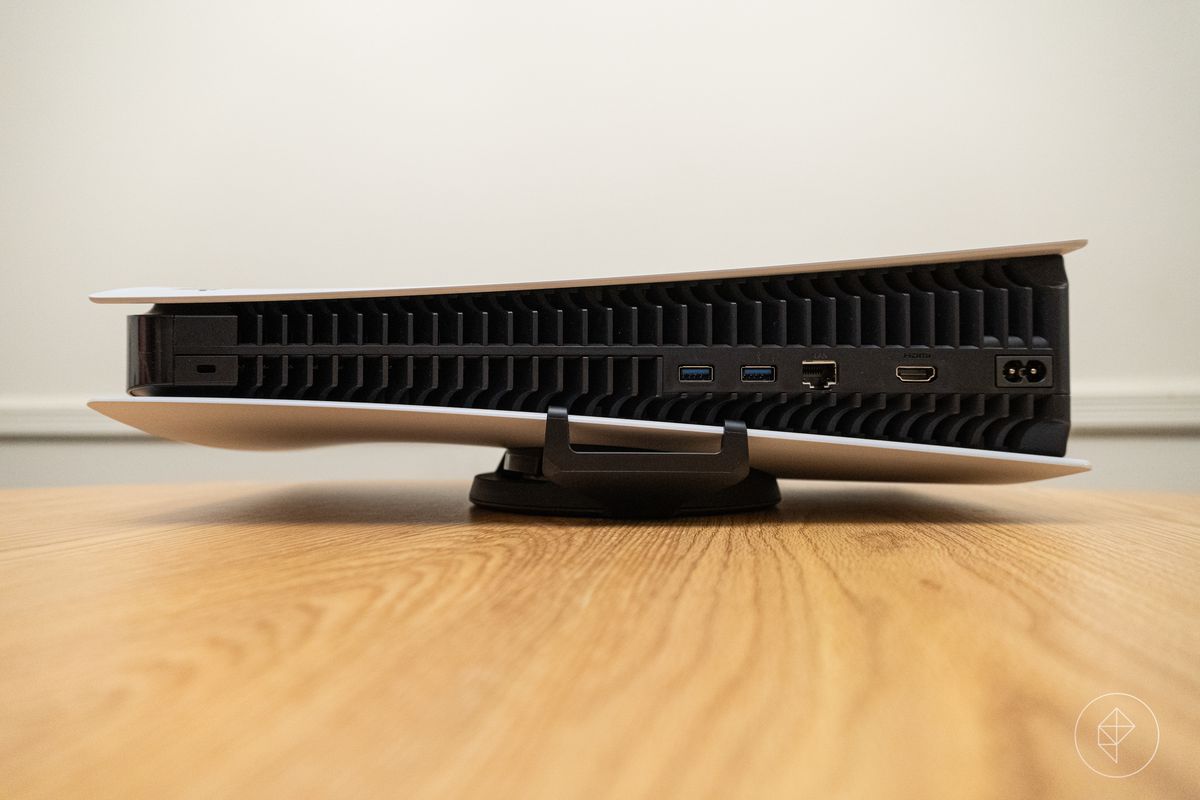 PlayStation 5 ligger i sin horisontella orientering på ett träbord, sett bakifrån, med stativets krokar synliga