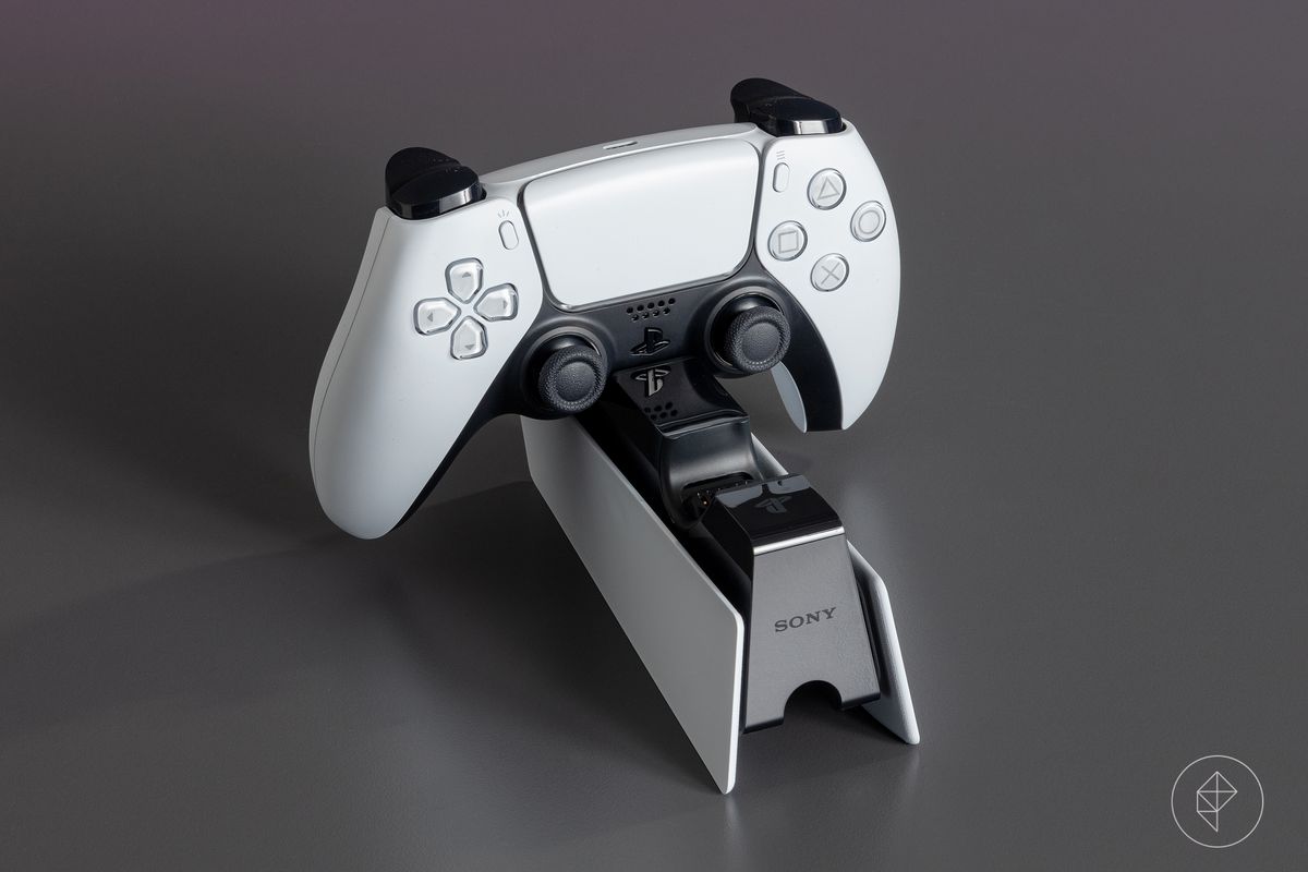 En PS5-kontroller vilar i en laddningshållare (ingår inte i konsolen)