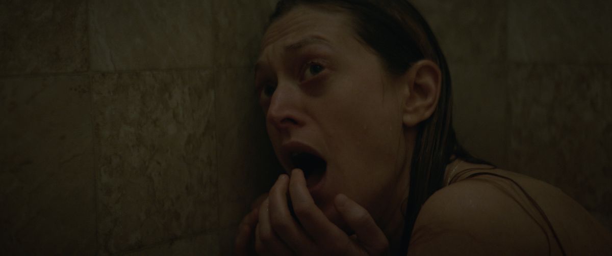 En våt kvinna krökt i duschen skriker och tittar på något utanför skärmen