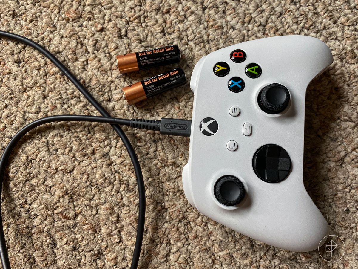 ett overhead-skott av Xbox Series S-kontroller som sitter på beige matta bredvid ett par AA-batterier, med en Nintendo-märkt USB-C-kabel ansluten till den