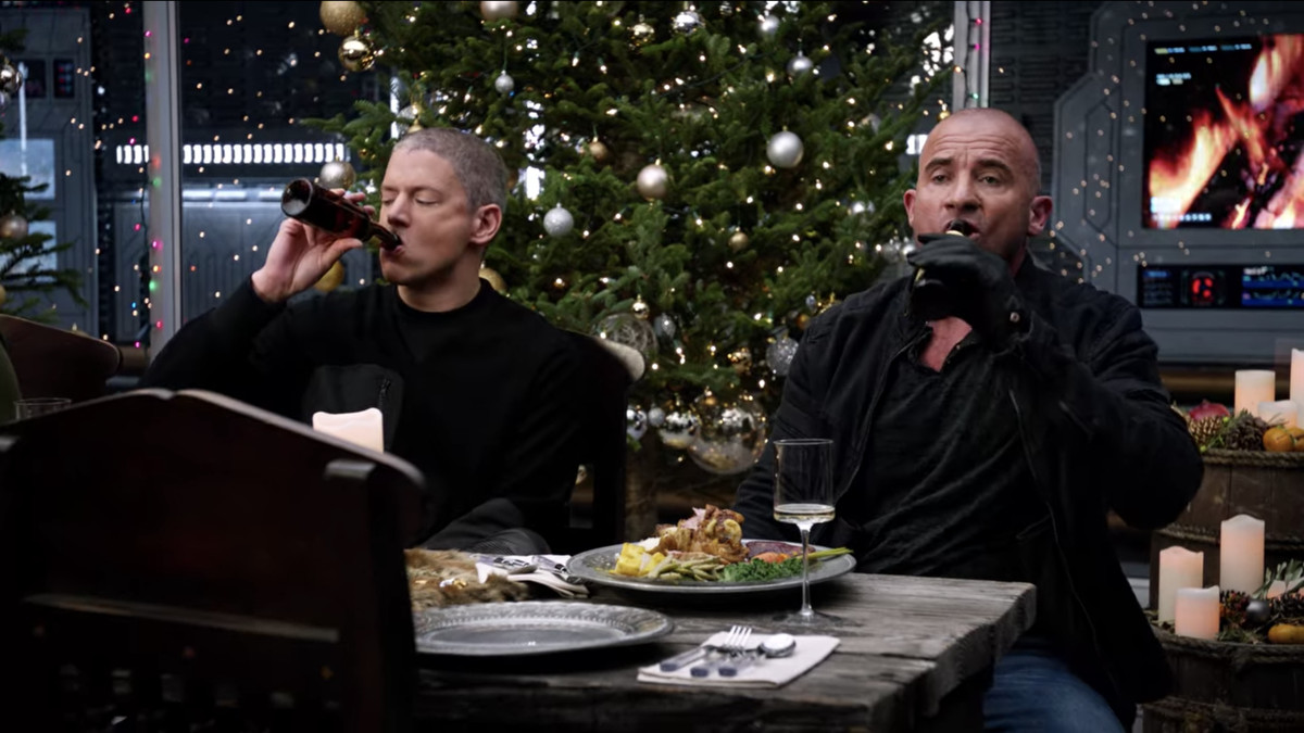 Captain Cold (Wentworth Miller) and Heat Wave (Dominic Purcell) knock back beers at the Christmas dinner table in Legends of Tomorrow. 