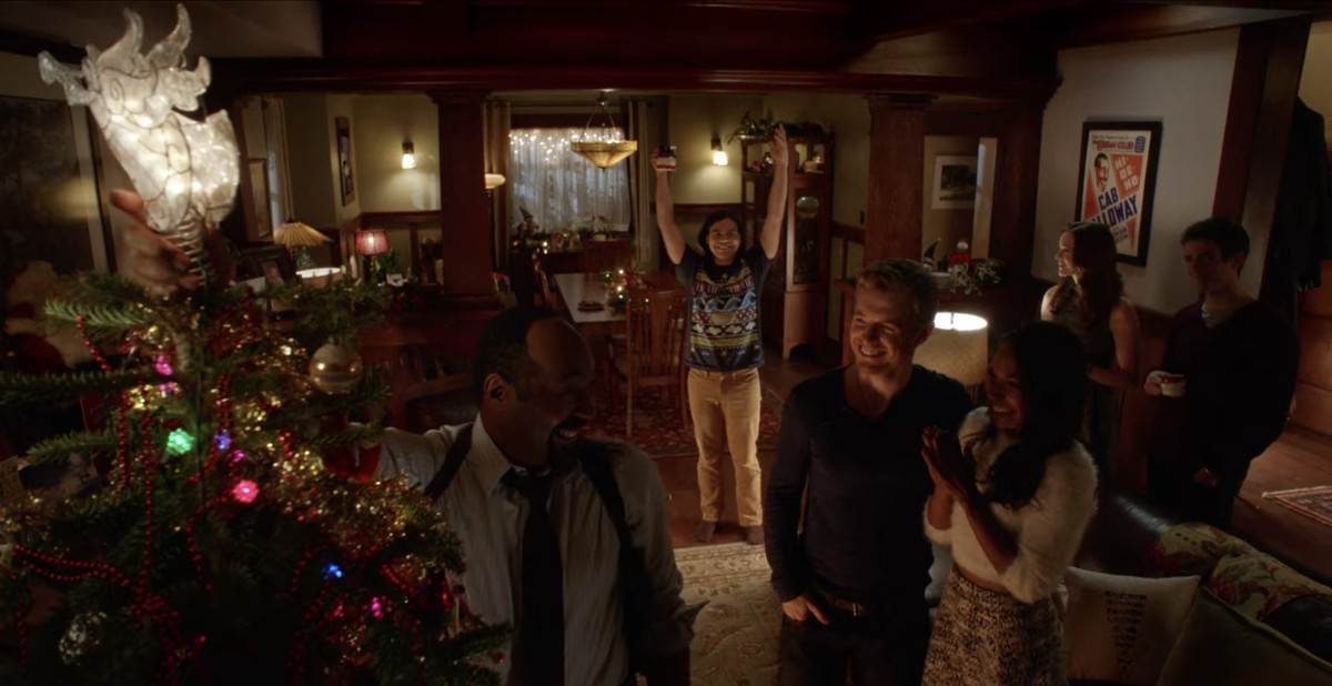 The West family celebrates Christmas with friends, cheering as Joe West (Jesse L. Martin) tops the family tree with an angel in The Flash. 